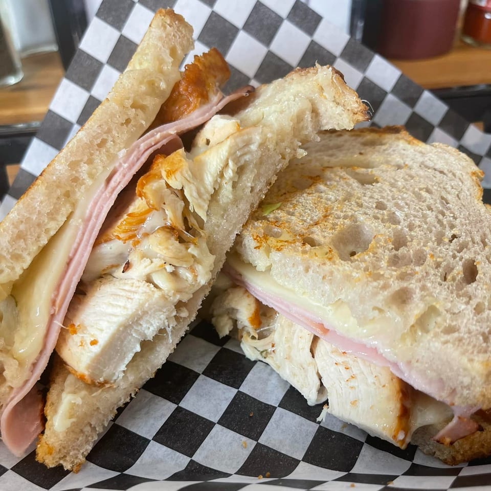 A Grinders Soups and Subs sandwich with chicken, ham, and melted cheese on toasted bread.