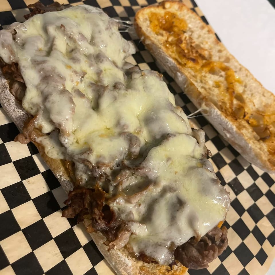 A Grinders Soups and Subs Philly cheesesteak sandwich with melted cheese and a side of toasted bread.